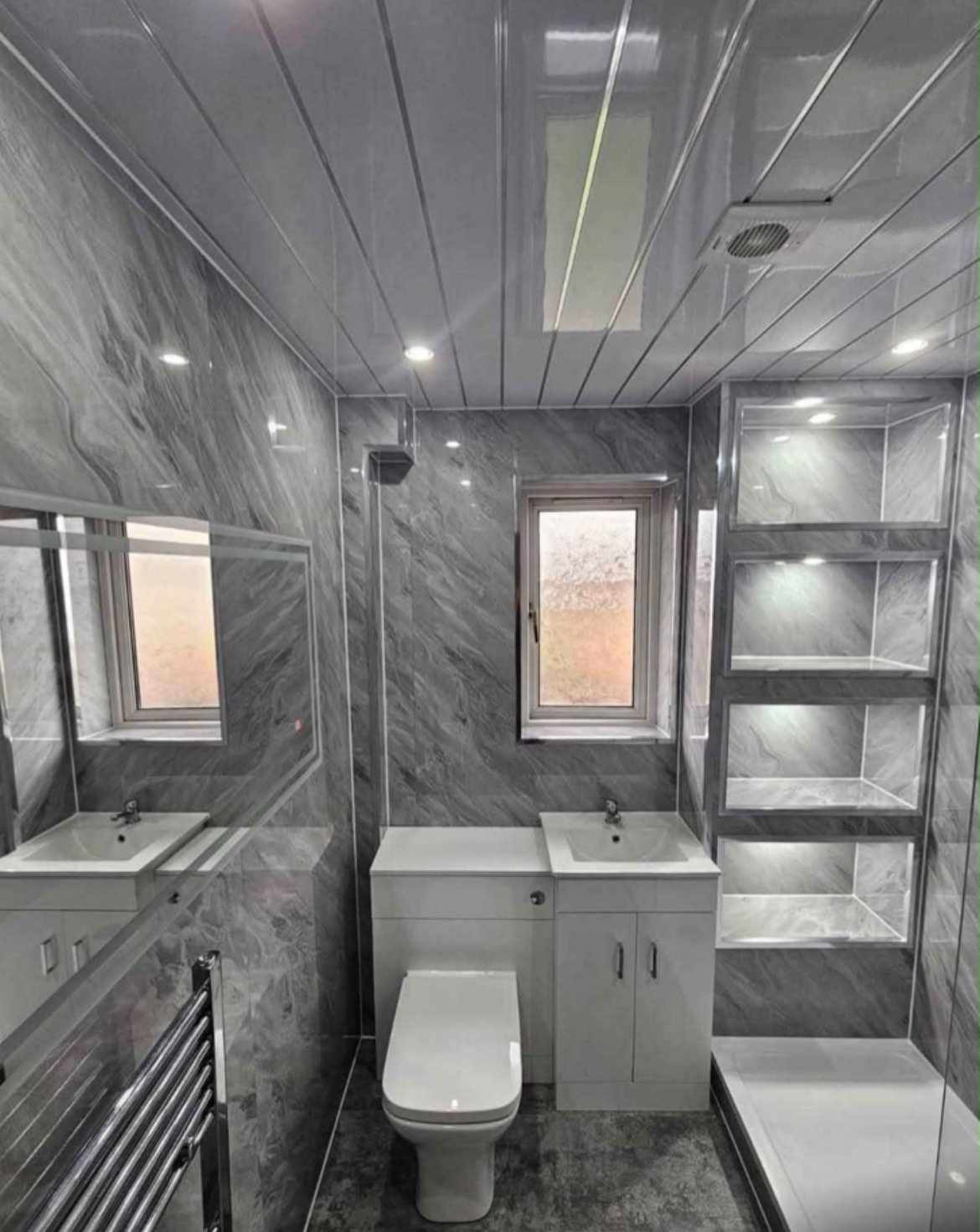 Modern gray bathroom with marble-effect tiles, toilet, sink vanity, walk-in shower with glass enclosure, and built-in shelving.