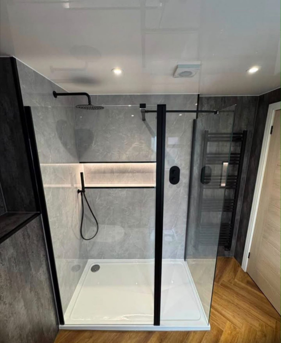 Modern bathroom shower enclosure with black frame, gray tile walls, rainfall showerhead, and white base tray
