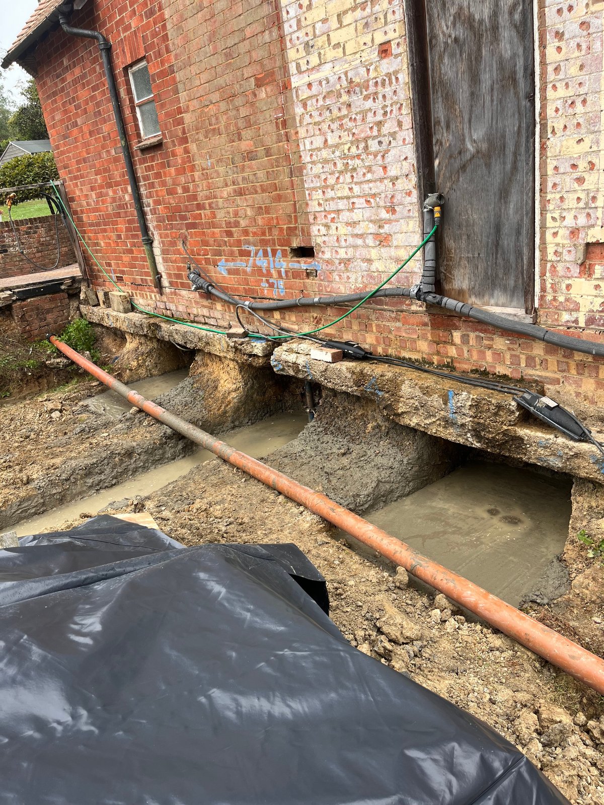 Brick building foundation with exposed pipes and black membrane lining concrete trenches during construction work