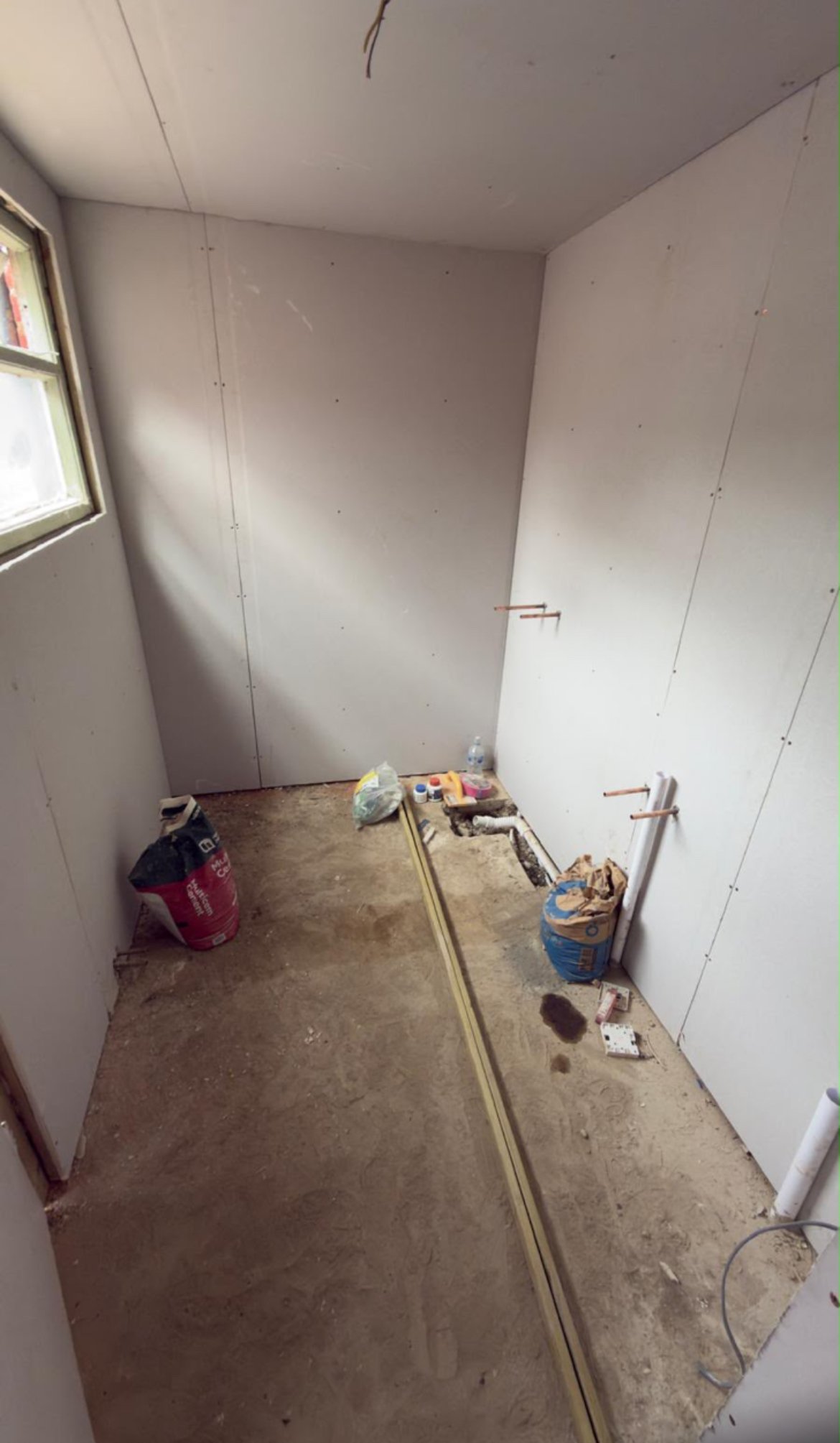 Unfinished drywall room under construction with concrete floor, electrical conduit, and construction materials in corner